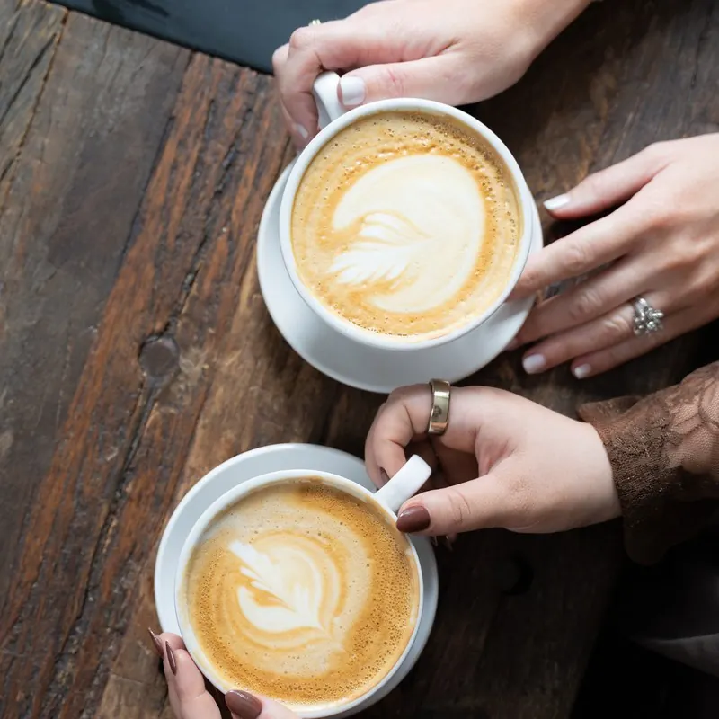 Two lattes passed across a wooden table