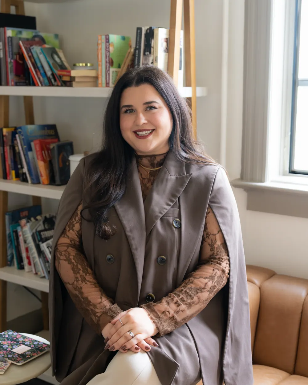 McKenzie Jevnikar smiling on a leather sofa in a brown cape blazer