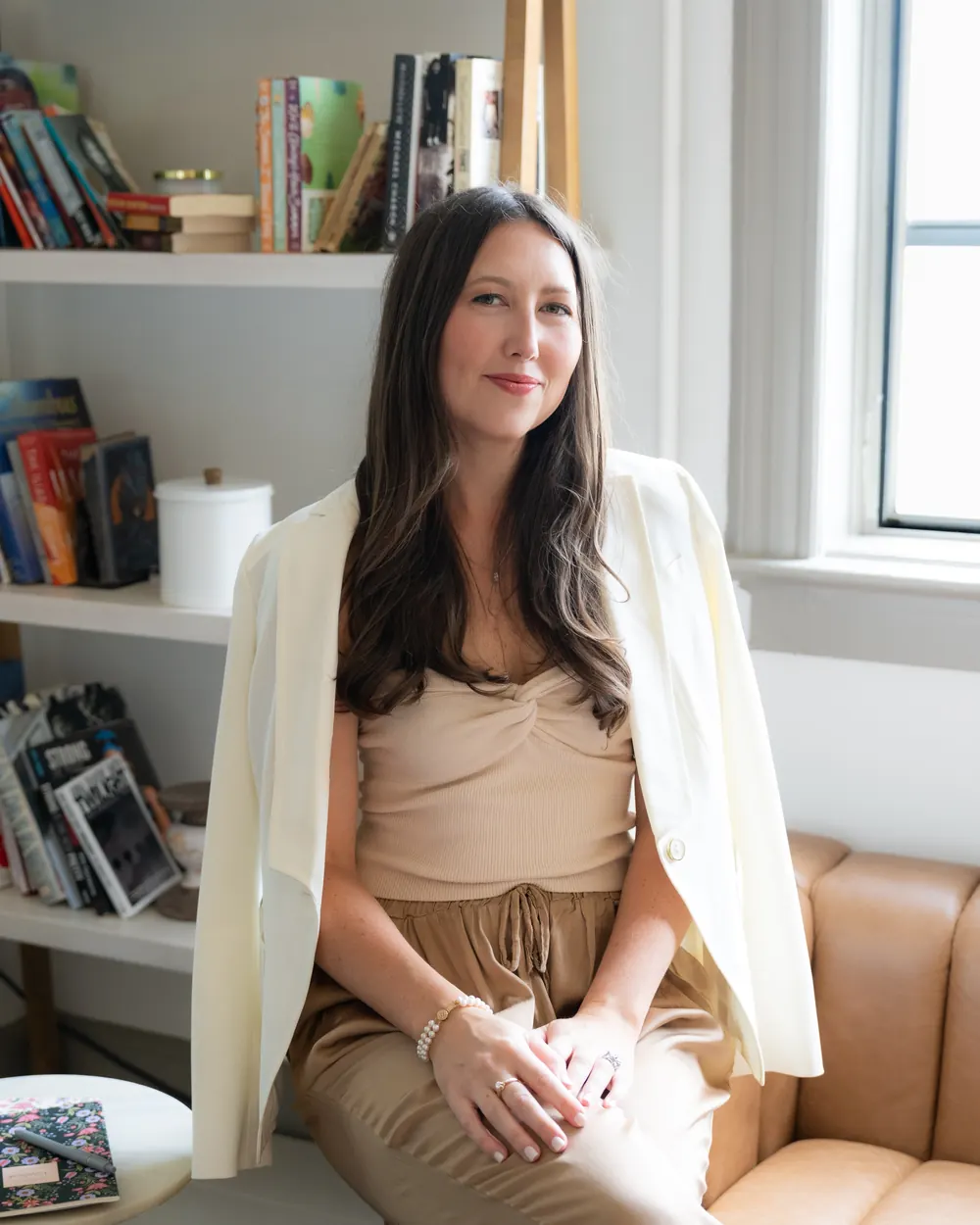 Sallie Micula smiling in a cream blazer in front of a bookshelf